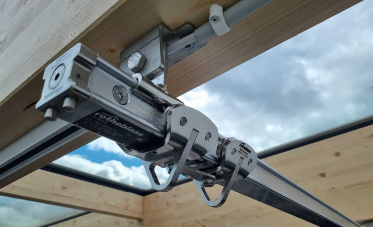 Rothoblaas H-RAIL rigid fall arrest rail system mounted on a glulam timber beam — sliding runner detail on a large-span timber and glass roof structure, Denmark.